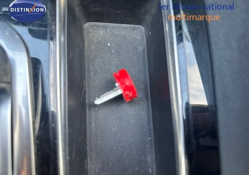 Gros plan sur la clé rouge posée dans le rangement central intérieur d'un Peugeot 3008 blanc nacré 2022.