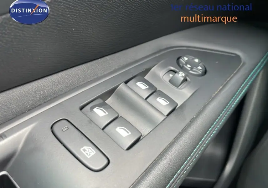 Gros plan sur les commandes des vitres électriques côté gauche, avec surpiqûres bleues sur la garniture noire.