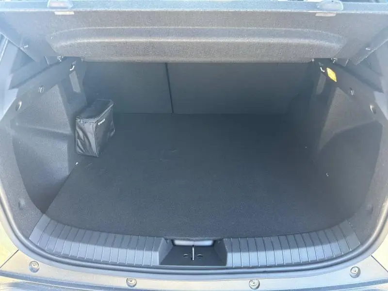 Coffre ouvert vu de face du Dacia Duster 1.2 hybrid-G vert cèdre, espace de chargement vide avec petite trousse noire sur le côté.