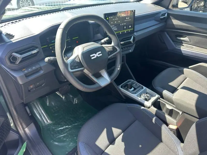 Vue intérieure avant droite du Dacia Duster 2026, tableau de bord noir avec écran tactile et volant multifonction.