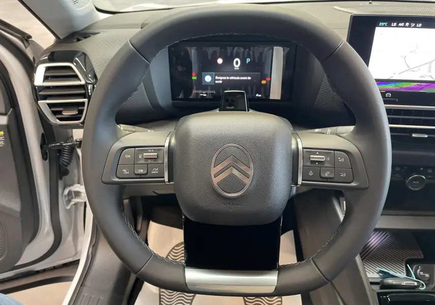 Vue rapprochée du volant cuir noir et du tableau de bord numérique d'une Citroën C4 blanche, intérieur moderne.