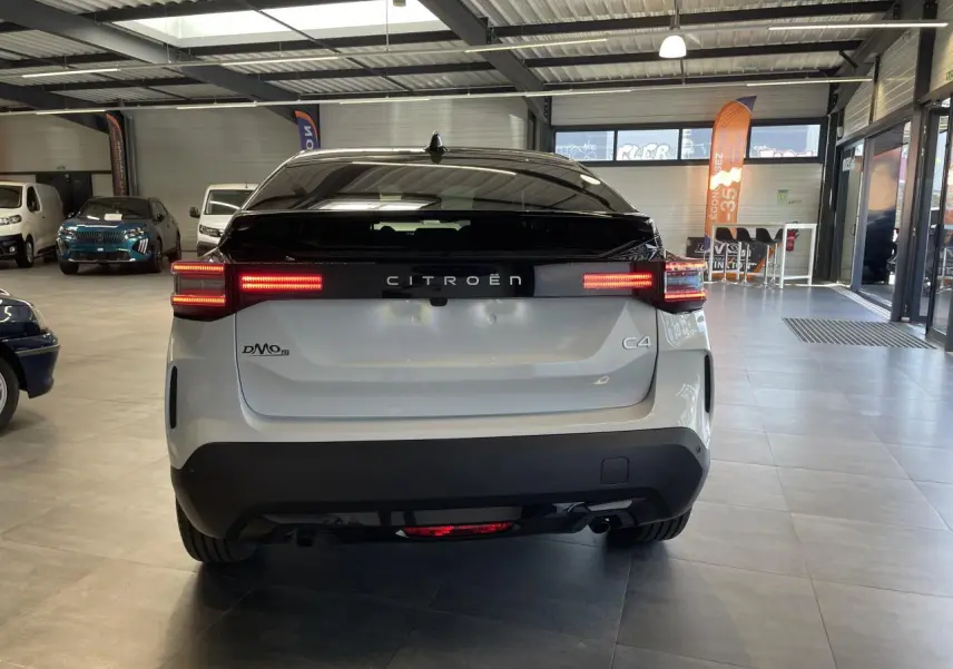 Vue arrière d'une Citroën C4 blanche avec toit noir Perla Nera et feux arrière LED allumés en intérieur showroom.