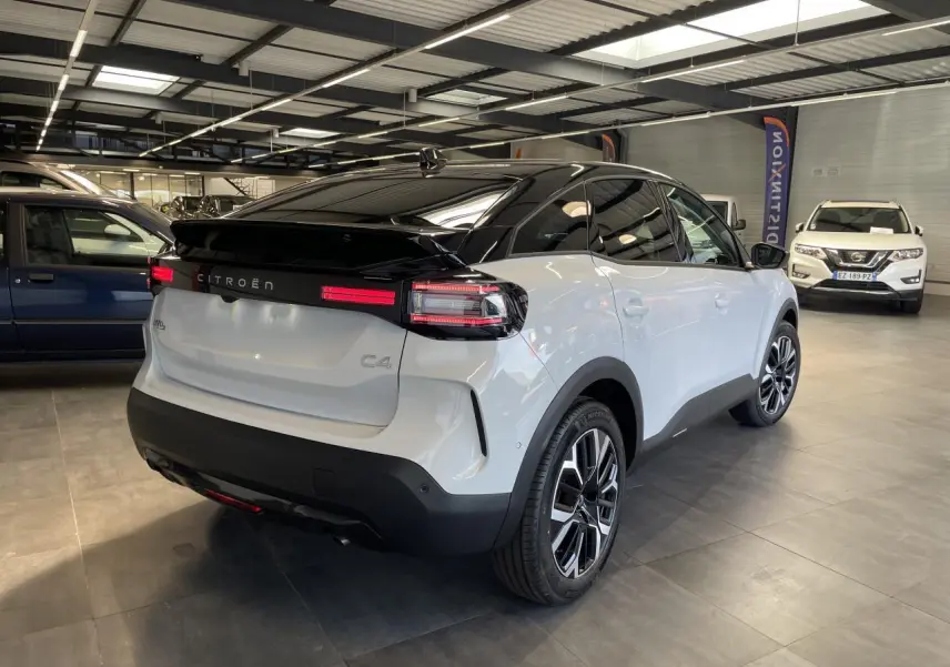 Vue 3/4 arrière droite d'une Citroën C4 blanche avec toit noir et jantes alliage 18 pouces en showroom.