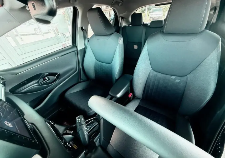 Intérieur de la Toyota Yaris Hybrid 2025 vu côté conducteur, sièges tissu gris et noir avec accoudoir central.