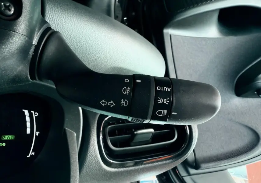 Gros plan sur la manette des feux et clignotants à gauche du volant dans l'habitacle noir d'une Toyota Yaris hybride 2025.