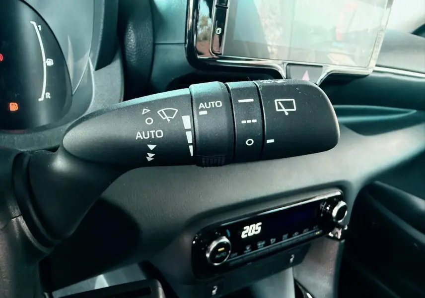 Gros plan sur la commande d'essuie-glace à gauche du volant dans l'habitacle noir de la Toyota Yaris Hybrid 2025.