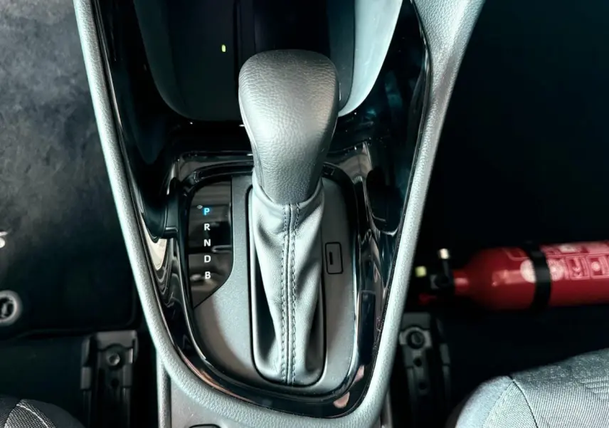 Le levier de vitesse automatique noir de la Toyota Yaris Hybrid 2025 vu de dessus avec un extincteur rouge à côté.