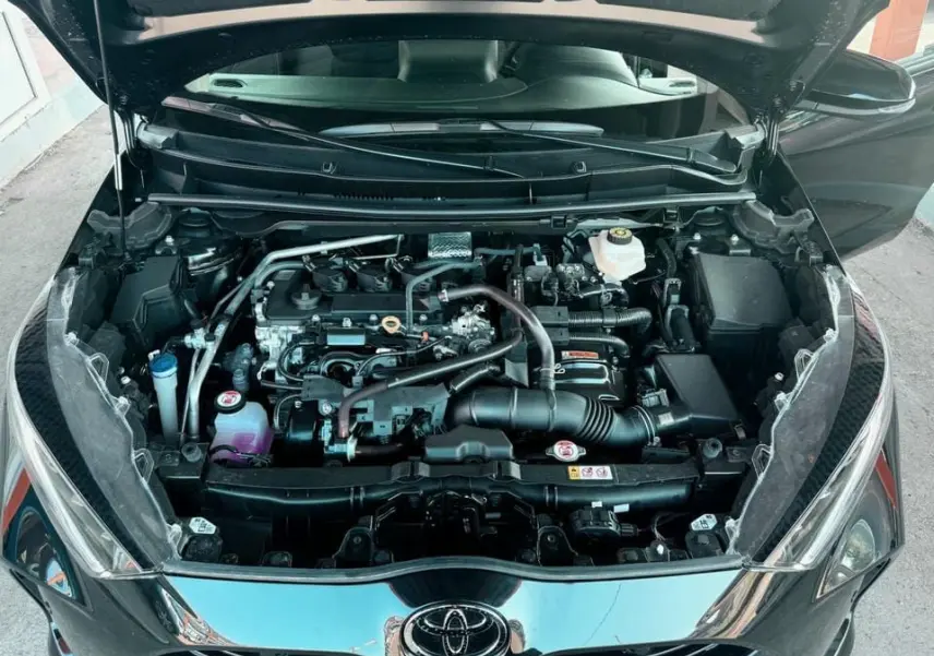 Vue plongeante sur le moteur d'une Toyota Yaris noire avec capot ouvert, montrant les composants du compartiment moteur.