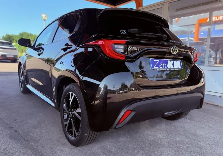 Vue 3/4 arrière droite d'une Toyota Yaris hybride noire 2025 avec feux arrière LED et jantes noires.