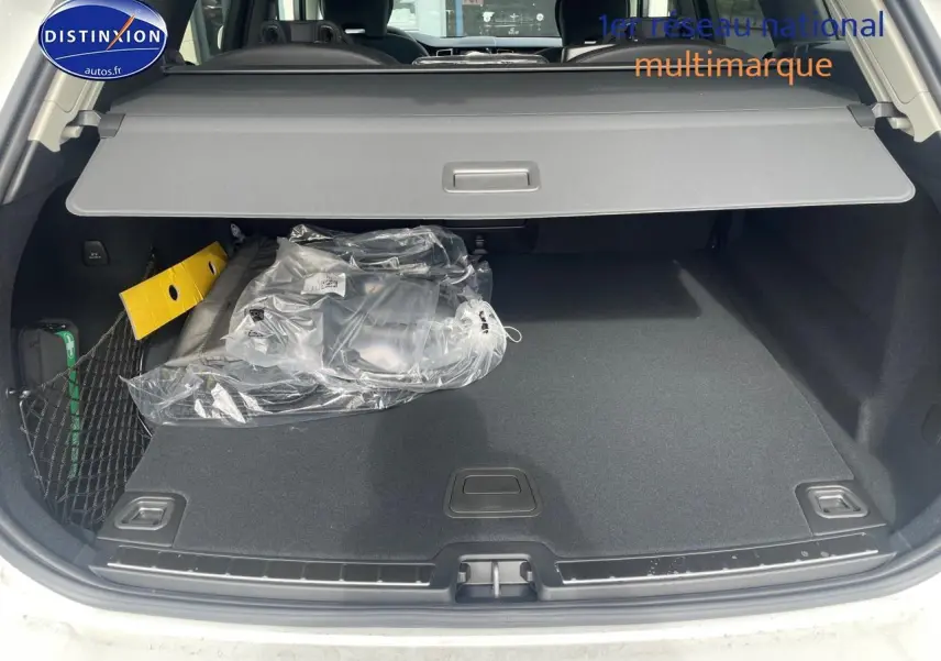 Coffre ouvert d'un Volvo XC60 gris 2024, montrant la tablette cache-bagages et un filet de rangement latéral.