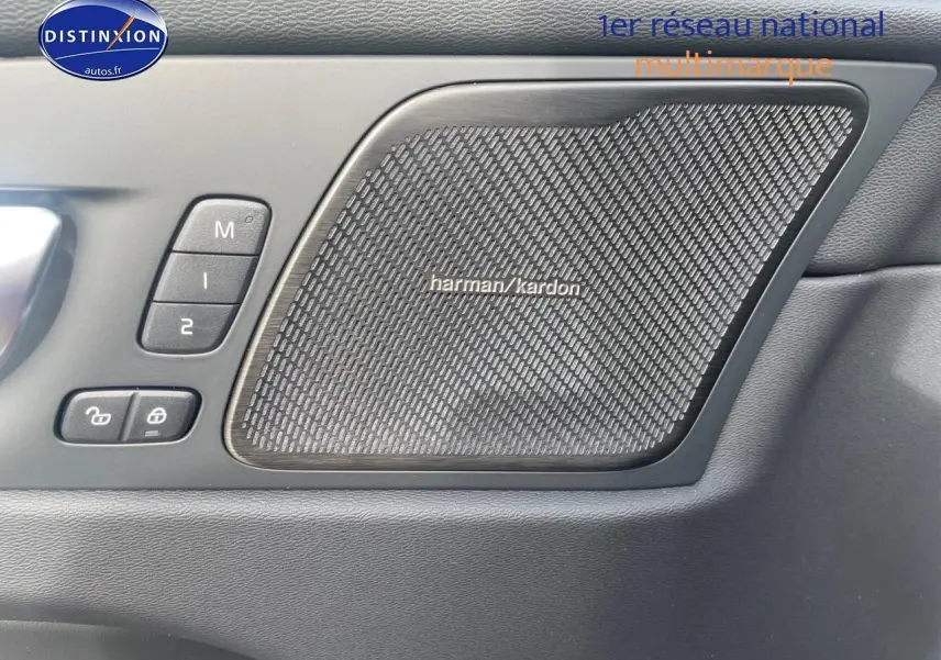 Gros plan sur la porte avant gauche du Volvo XC60 gris, mettant en valeur l'enceinte Harman Kardon et les commandes mémoire sièges.