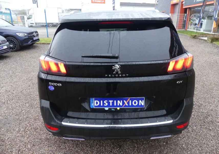Vue arrière d'un Peugeot 5008 GT noir métallisé avec feux arrière LED allumés et double sortie d'échappement chromée.
