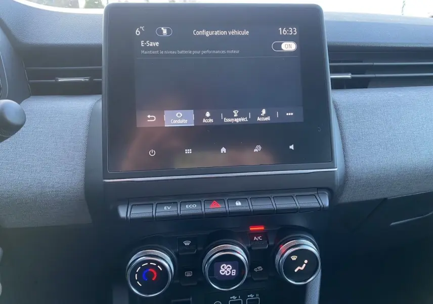 Vue intérieure centrée sur l’écran tactile et les commandes de climatisation d’une Renault Clio V gris schiste.