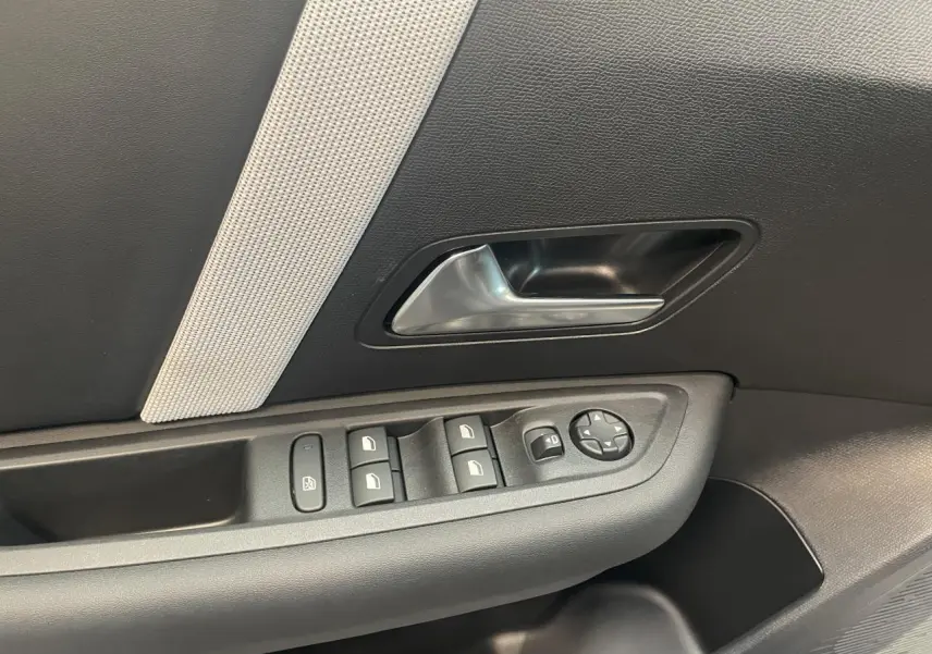 Gros plan sur la porte côté gauche de la Citroën C4 gris, montrant la poignée intérieure et les commandes des vitres électriques.