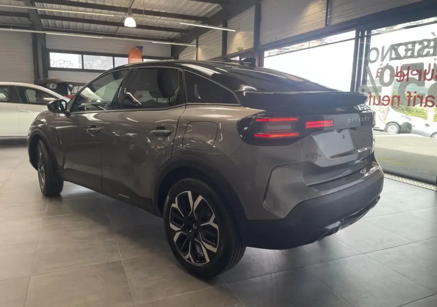 Vue 3/4 arrière droite d'une Citroën C4 gris métallisé avec toit noir et jantes alliage 18 pouces en showroom.