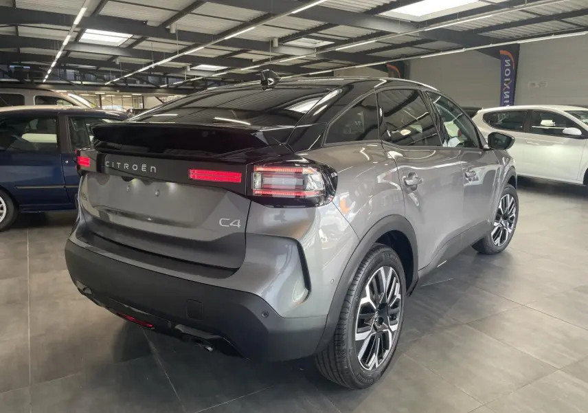 Vue 3/4 arrière droite d'une Citroën C4 gris métallisé avec toit noir et feux arrière LED en intérieur showroom.