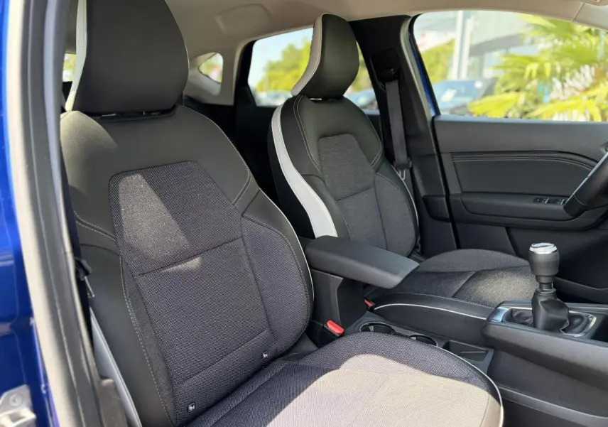 Vue intérieure côté conducteur du Renault Captur 2024, sièges bi-matière gris et noir avec accoudoir central.