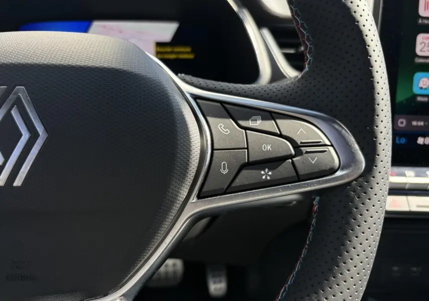 Gros plan sur le volant perforé du Renault Symbioz gris Rafale, avec commandes intégrées et surpiqûres tricolores.