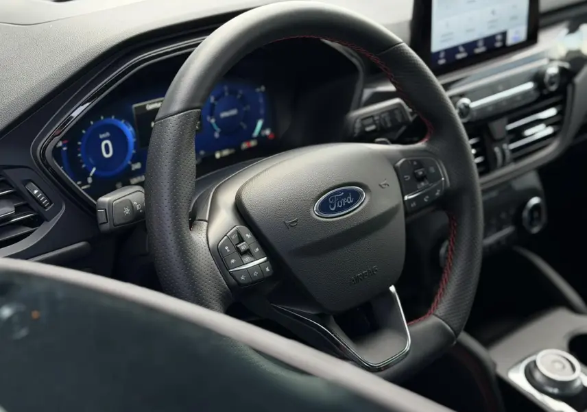 Vue rapprochée du volant noir avec surpiqûres rouges du Ford Kuga 2023, tableau de bord numérique et console centrale visible.