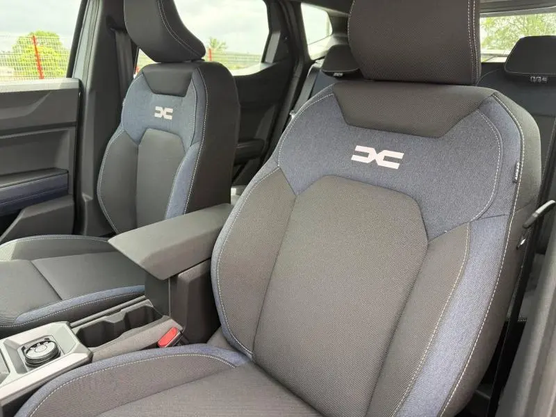 Vue rapprochée des sièges avant en tissu noir et bleu Denim du Dacia Duster 1.2 hybrid-G 150ch Expression 4x4, avec accoudoir central.