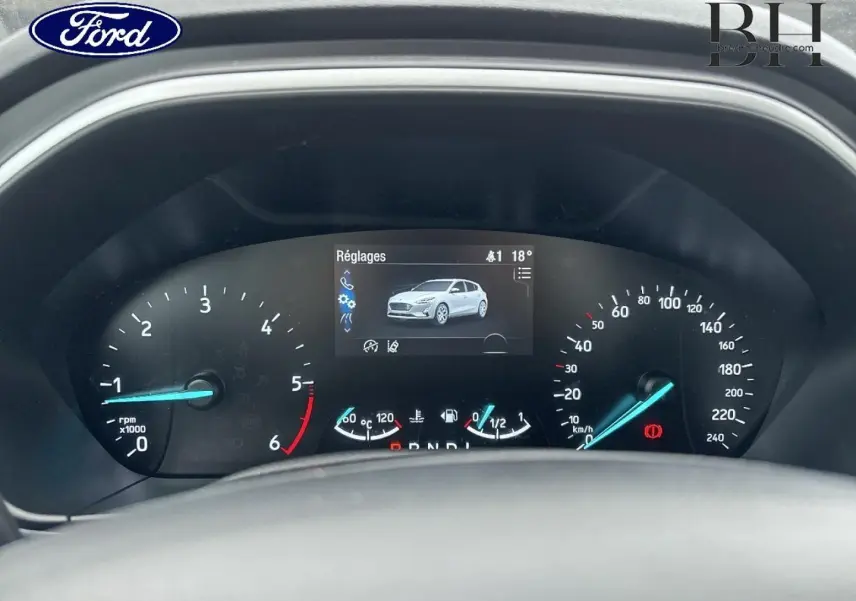 Vue rapprochée du tableau de bord de la Ford Focus 2020, affichage numérique avec indicateurs bleus et image véhicule blanche.