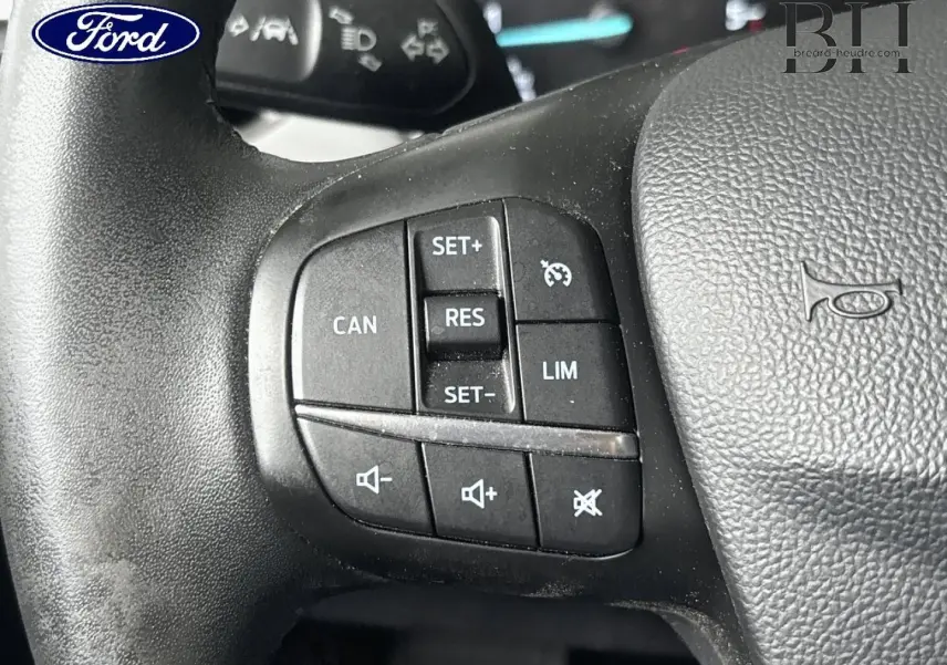 Gros plan sur les commandes du volant cuir noir d'une Ford Focus bleu azur métallisé, boutons multifonctions visibles.