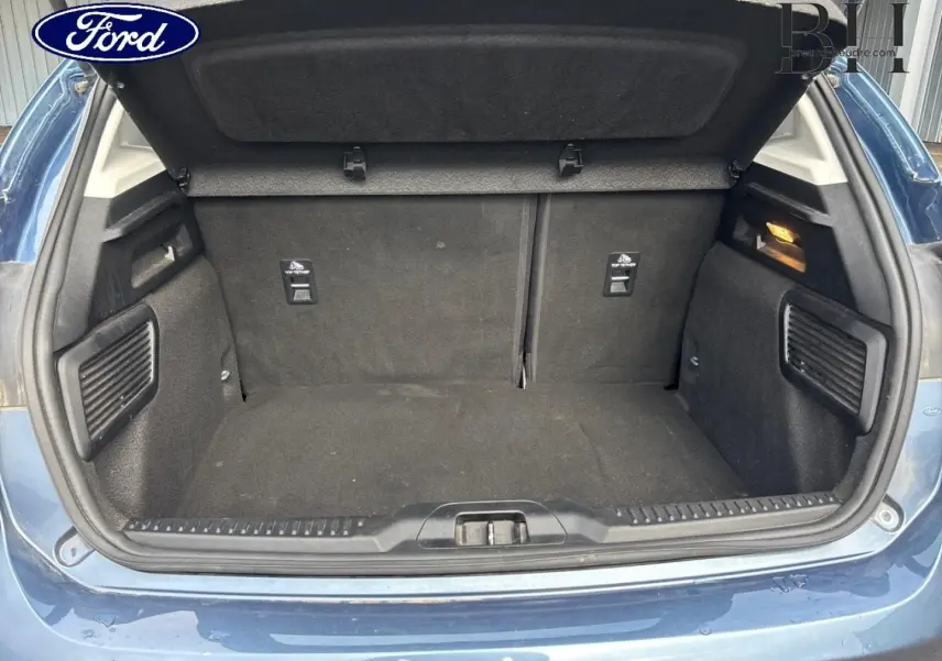 Coffre ouvert vu de l'arrière d'une Ford Focus bleu azur métallisé, montrant l'espace de chargement vide.