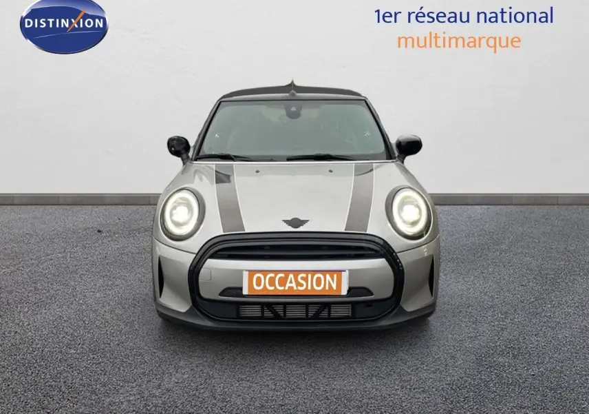 Vue frontale d'une MINI Cabriolet 2023 couleur Melting Silver Metal avec phares allumés et bandes noires sur le capot.