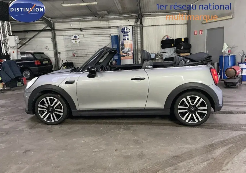 Profil droit d'une MINI Cabriolet 2023 couleur Melting Silver Metal avec capote ouverte dans un garage.