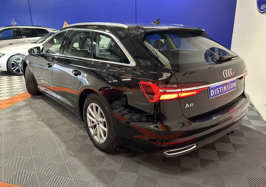 Audi A6 Avant noire vue 3/4 arrière droit dans un showroom avec feux arrière allumés et jantes argentées.