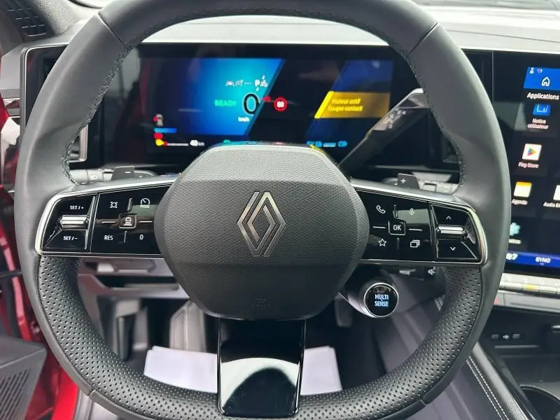 Vue rapprochée du volant multifonction Renault Austral rouge flamme 2025 avec tableau de bord numérique et écran tactile.