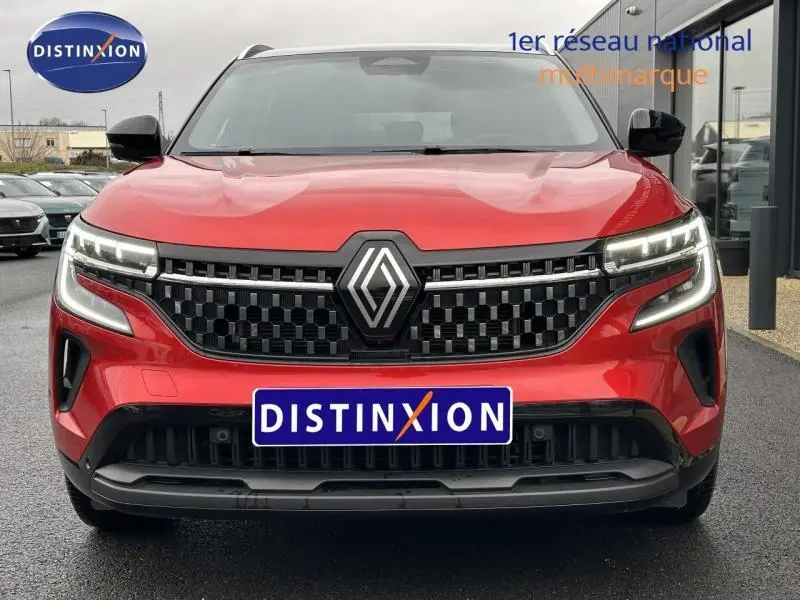 Vue frontale d'un Renault Austral 2025 rouge flamme avec calandre noire à damier et feux LED distinctifs allumés.