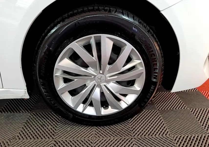 Gros plan sur la roue avant droite d'une Peugeot 208 blanche, mettant en valeur la jante alliage et le pneu Michelin.
