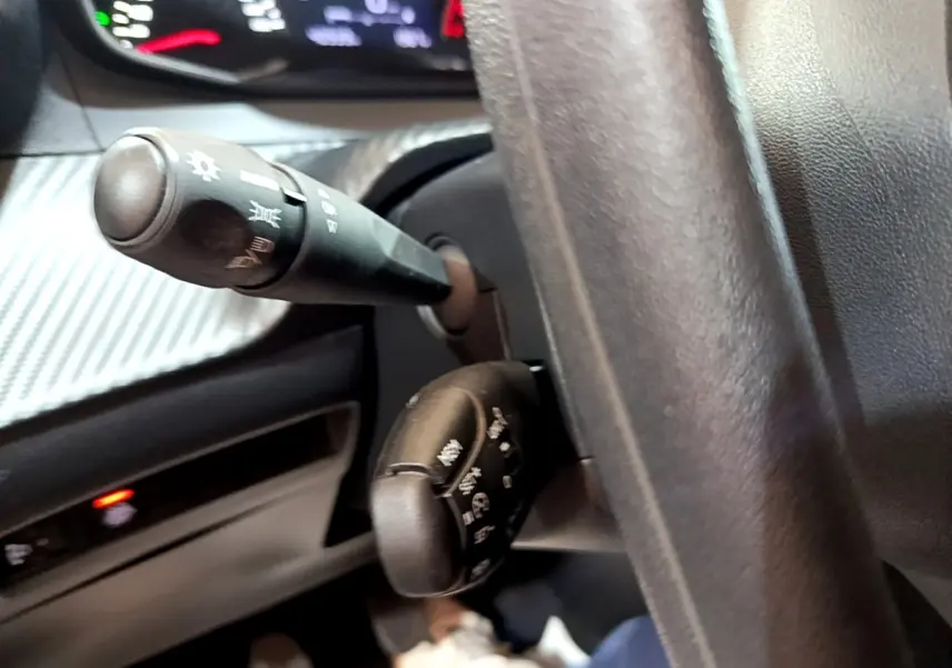 Gros plan sur les commandes au volant et le tableau de bord noir de la Peugeot 208 blanche, version 1.5 BlueHDi 100 S&S Premium.