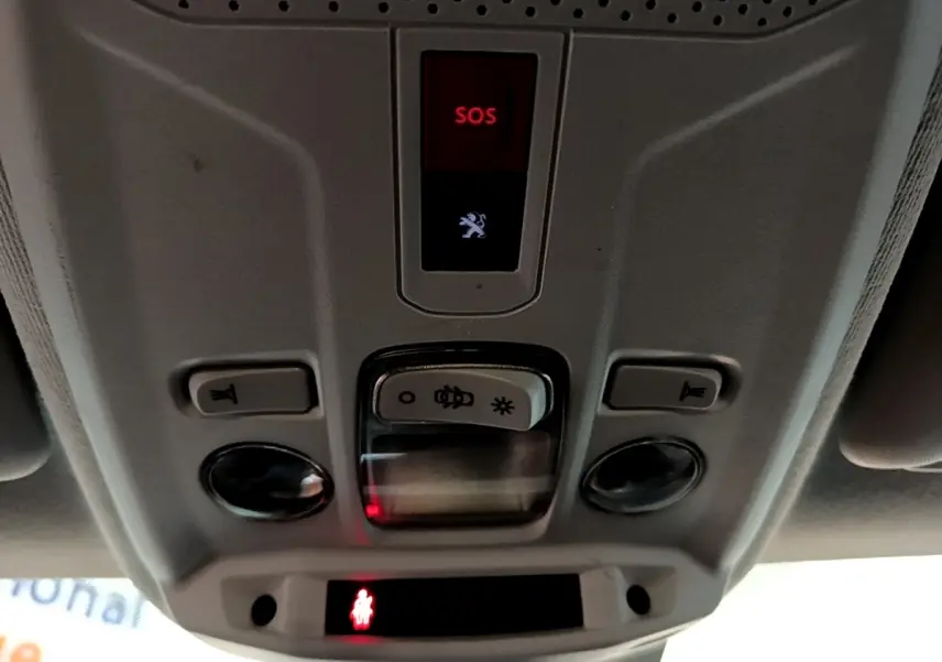 Vue en contre-plongée du panneau de commandes plafond gris clair de la Peugeot 208 blanc, avec bouton SOS rouge allumé.