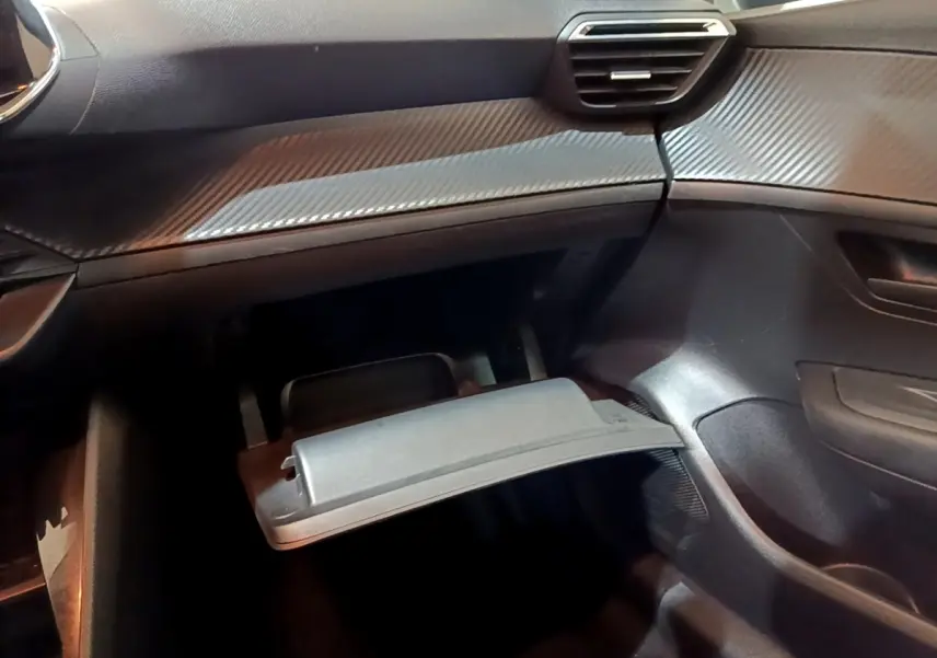 Intérieur de la Peugeot 208 1.5 BlueHDi 2022, vue du coffre à gants ouvert côté passager, tableau de bord noir.