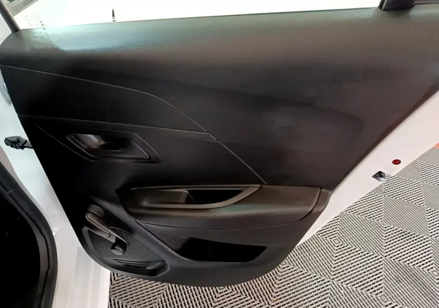 Vue intérieure de la porte avant gauche noire d’une Peugeot 208 blanche, avec poignée et commande de vitre manuelle.