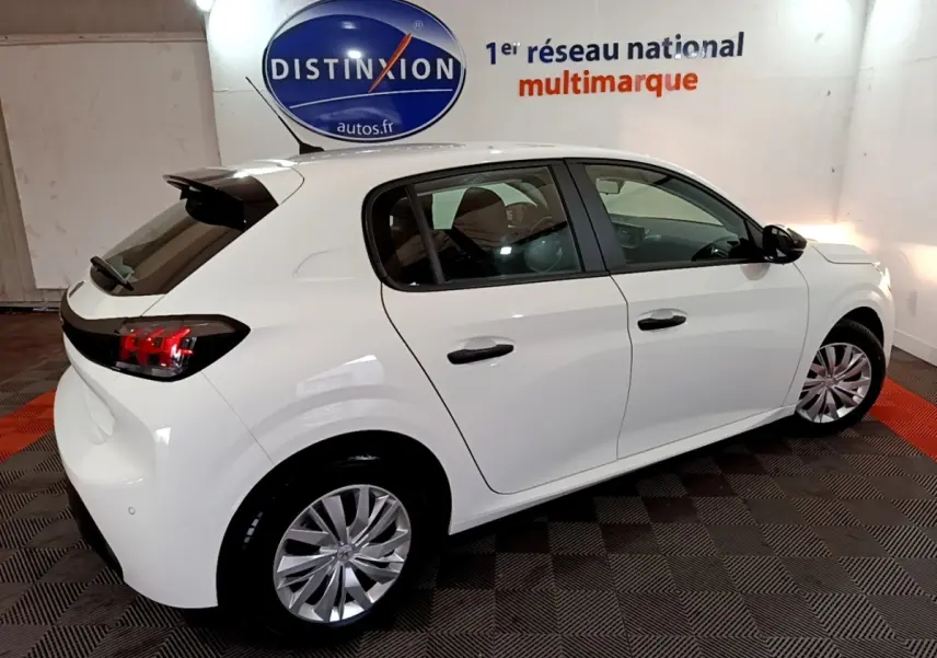 Vue 3/4 arrière droite d'une Peugeot 208 blanche 2022, avec jantes alliage et vitres teintées en intérieur showroom.