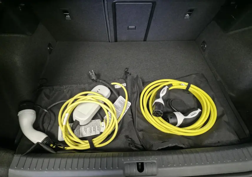 Coffre ouvert d'une CUPRA Formentor 1.4 e-Hybrid 2023 avec câbles de recharge jaune rangés sur tapis noir.