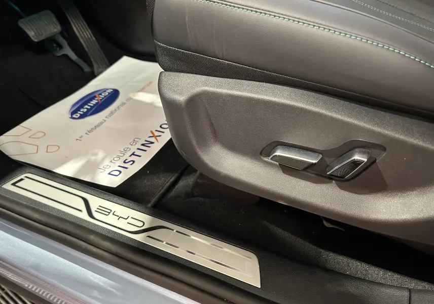 Gros plan sur la commande de réglage du siège en cuir noir et la plaque de seuil BYD côté conducteur, intérieur lumineux.