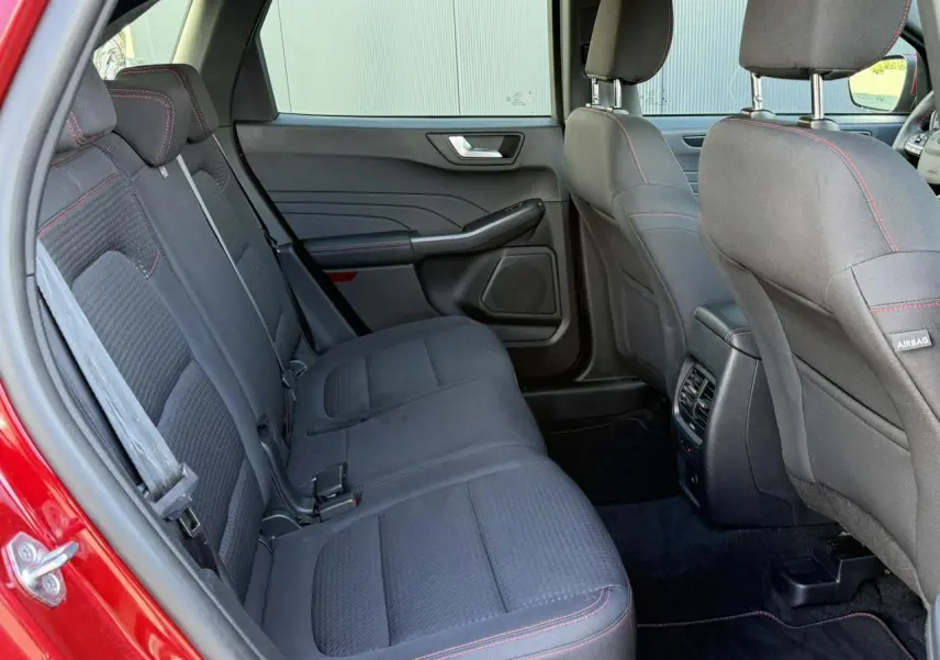 Vue intérieure arrière côté gauche du Ford Kuga rouge Lucifer 2024, sièges tissu noir avec surpiqûres rouges et appuie-têtes réglables.