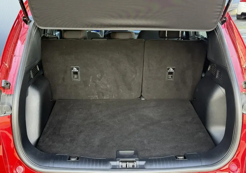 Coffre ouvert du Ford Kuga 2.0 EcoBlue rouge Lucifer, montrant l’espace de chargement arrière vide et les dossiers de sièges rabattus.