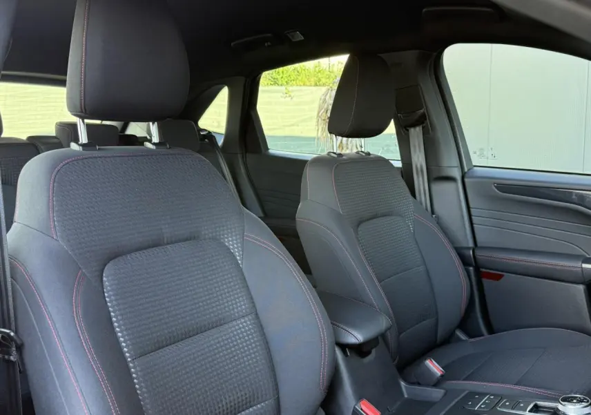 Vue intérieure avant du Ford Kuga 2024, sièges noirs avec surpiqûres rouges et console centrale avec sélecteur rotatif.