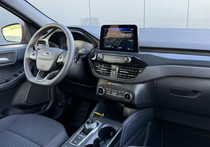 Vue intérieure côté conducteur du Ford Kuga 2024 avec volant ST-Line à surpiqûres rouges et écran tactile central.