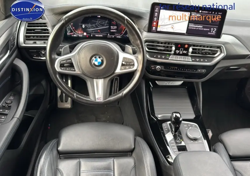 Vue intérieure centrée sur le volant cuir multifonction et la console centrale noire brillante d'une BMW X4 noire.