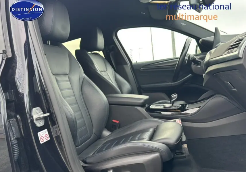 Intérieur avant côté conducteur d’une BMW X4 noire, sièges sport cuir noirs et console centrale avec accoudoir.