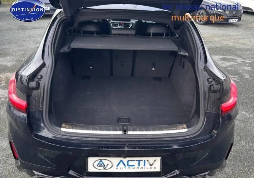 Vue arrière ouverte du coffre d'un BMW X4 noir (g02) xdrive30d 286 m sport avec feux arrière LED allumés.