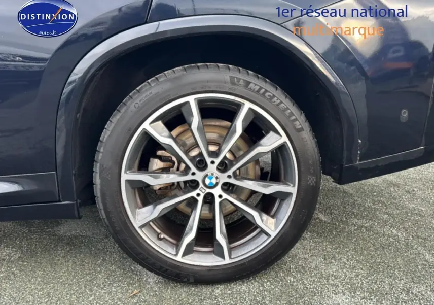 Gros plan sur la roue arrière droite d’un BMW X4 noir avec jante alu à dix branches.
