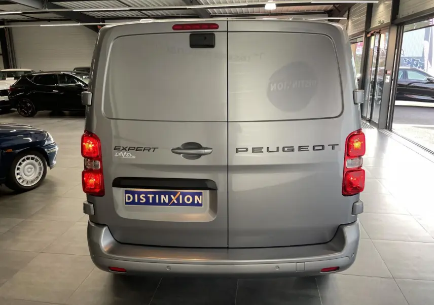 Vue arrière d'un Peugeot Expert Fourgon gris Artense avec portes battantes et feux allumés en intérieur showroom.
