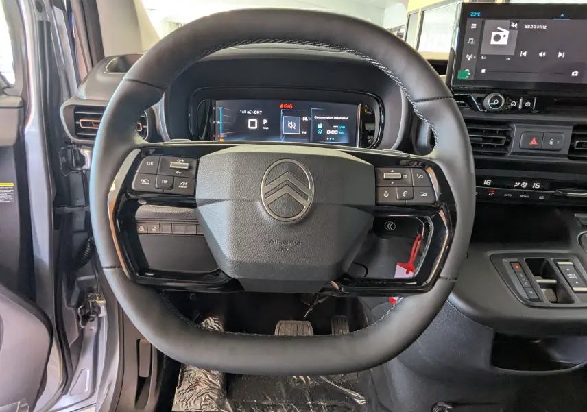Vue intérieure centrée sur le volant noir du Citroën Berlingo gris Artense avec tableau de bord digital et écran tactile.